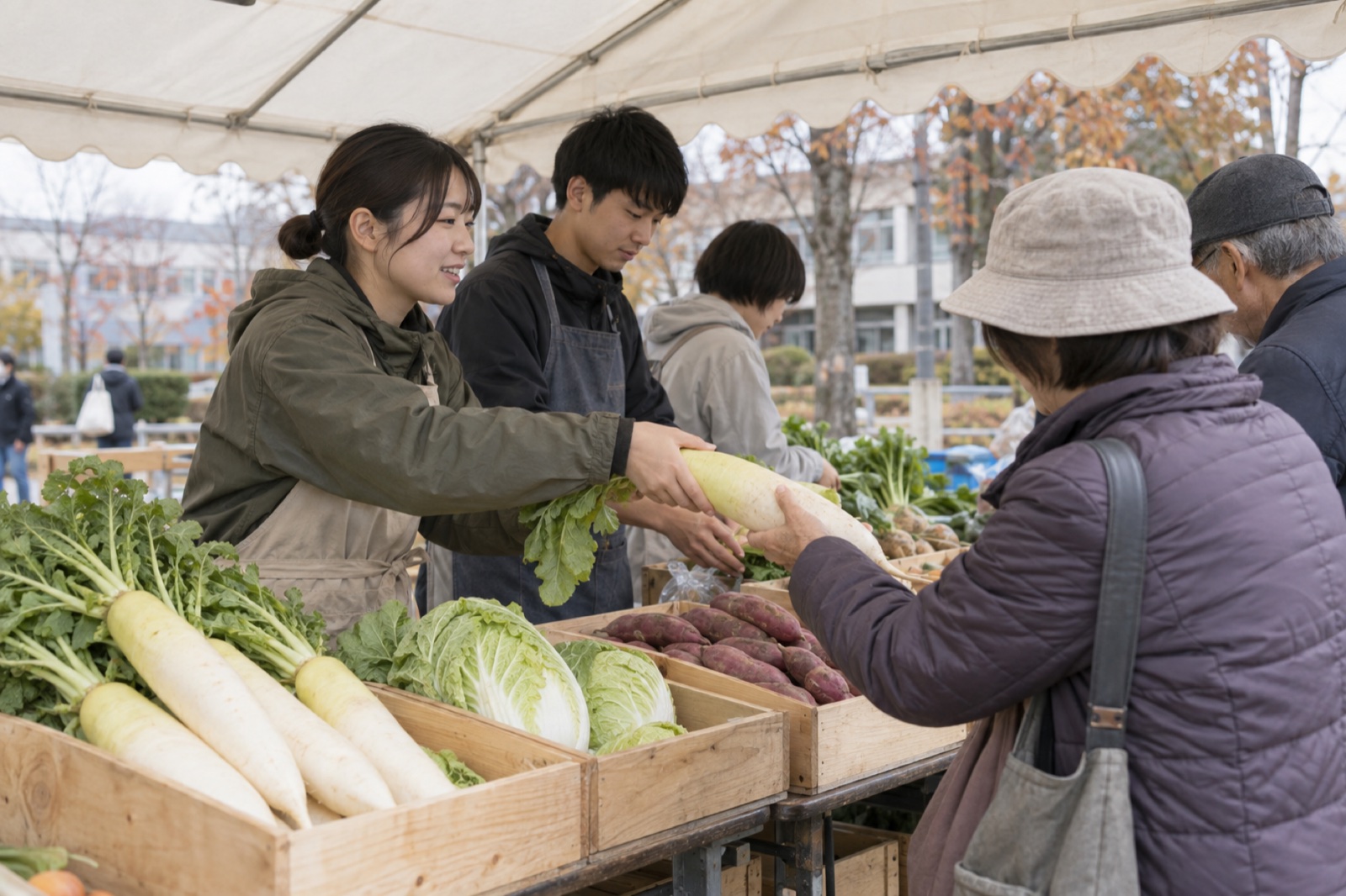 秋の収穫祭で、野菜を並べたテントで来場者に対応する学生
